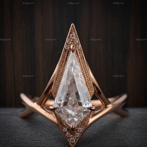 Puede incluir: Un anillo de oro rosa con una gran piedra central en forma de cometa engastada en un marco geométrico. El engaste está acentuado con pequeños diamantes redondos en pavé en las puntas superior e inferior, con un detalle de borde milgrain.