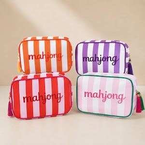 Può includere: Quattro astucci rettangolari con cerniera a righe verticali arancioni, viola, rosse e rosa. Ogni astuccio presenta la parola mahjong ricamata in un colore coordinato sul davanti e include una nappa decorativa attaccata alla cerniera laterale.