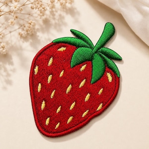 May include: A strawberry-shaped embroidered patch featuring a vibrant red body with yellow stitched seeds and a bright green stem and leaves at the top. The patch has a defined border and a textured surface created by dense thread work.