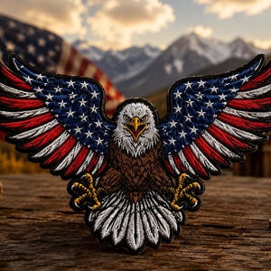 May include: An embroidered patch featuring a bald eagle with wings spread wide. The wings display a pattern of red and white stripes with a blue field containing white stars. The eagle has a white head, brown body, and yellow talons extended forward.