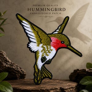 May include: An embroidered patch featuring a hummingbird with olive green wings, a bright red throat, and white underparts. The patch is labeled with the text PREMIUM QUALITY HUMMINGBIRD EMBROIDERED PATCH. The design shows the bird in flight.