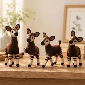 May include: Four needle-felted okapi figurines standing in a row. Each animal has a dark brown body, a cream-colored face, and cream-colored legs with dark brown horizontal stripes. They feature small ears, black noses, and dark eyes.