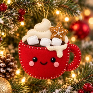 May include: A felt Christmas ornament shaped like a red mug with a smiling face, filled with brown hot cocoa, white whipped cream, three white marshmallows, and a brown star-shaped cookie with white icing details, hanging by a gold string.