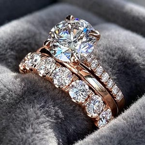 Könnte beinhalten: Ein Verlobungsring-Set aus Roségold mit einem großen, rund geschliffenen Mittelstein in einer Vier-Krappen-Fassung, ergänzt durch einen passenden Ehering. Beide Ringe sind mit einer Reihe kleinerer, rund geschliffener Steine besetzt.