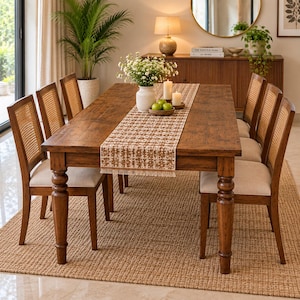 Puede incluir: Una mesa de comedor rectangular de madera con patas torneadas y seis sillas con respaldos de rejilla y asientos tapizados en beige. Un camino de mesa estampado, un jarrón blanco con flores, manzanas verdes y dos velas decoran la mesa.