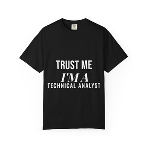 May include: A black short-sleeved t-shirt featuring white text printed on the chest that reads TRUST ME I'M A TECHNICAL ANALYST. The shirt has a crew neckline and a standard fit, with a small brand label visible on the inside of the collar area.