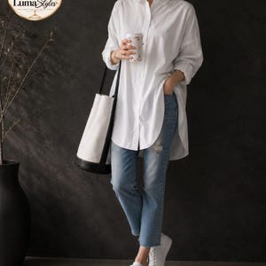 May include: An oversized white button-down shirt with long sleeves, paired with light blue distressed denim jeans and white sneakers. A white bucket bag with black trim and a white cup are held. The LumaStyles logo is visible in the top corner.