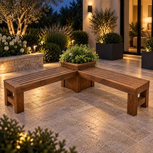 May include: An L-shaped wooden bench featuring a central square planter box. The bench is constructed from horizontal slats with a medium brown finish. A green leafy plant is situated in the center planter box, which connects the two bench sections.