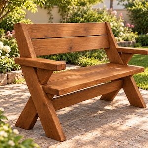 May include: A medium-brown wooden bench featuring a slatted backrest, a flat seat, and two armrests. The structure is supported by two X-shaped legs on each side, constructed from thick, sturdy planks with a visible wood grain finish throughout.