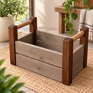 Puede incluir: Una caja de madera rectangular con paneles laterales horizontales teñidos de gris y cuatro postes esquineros verticales de color marrón oscuro. La caja incluye dos asas cilíndricas de madera clara que se extienden horizontalmente.