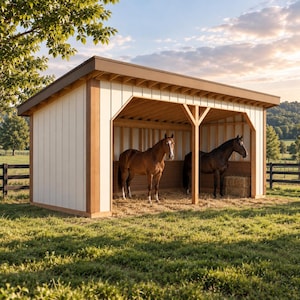 May include: A wooden horse shelter with cream-coloured vertical siding and brown trim, featuring an open front design with two stalls. Inside, a light brown horse and a dark brown horse stand on a straw-covered floor, with a hay bale in the corner.