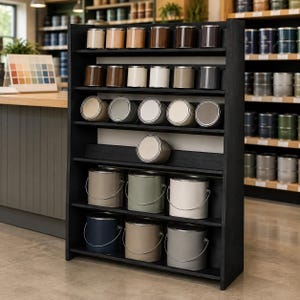 May include: A tall black wooden display shelf holding multiple rows of paint cans in various neutral shades. The top three shelves feature smaller cylindrical cans, while the bottom two shelves contain larger paint cans with metal handles.
