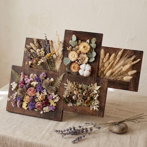 May include: A multi-panel dark wood wall art piece featuring four rectangular frames filled with dried flowers and botanicals, including purple roses, lavender, wheat stalks, cotton bolls, eucalyptus leaves, and various seed pods and moss.