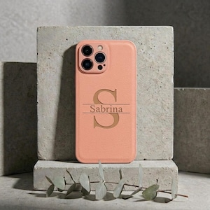 Peut inclure: Une coque de smartphone couleur pêche arborant une grande lettre S centrée avec le prénom Sabrina imprimé horizontalement au milieu. La coque présente une finition texturée et inclut des découpes pour les objectifs de l'appareil photo.