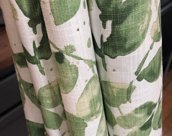 May include: A curtain panel featuring a white base fabric with a green watercolor-style leaf pattern. The fabric has a visible woven texture and is gathered into vertical folds, displaying a repeating botanical print of various green leaves.