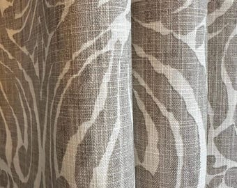 Może przedstawiać: Panel zasłonowy o tkanej fakturze materiału z dużym, powtarzającym się wzorem botanicznym w odcieniach taupe i złamanej bieli. Tkanina ma widoczny splot krzyżowy i układa się w miękkie, pionowe fałdy, tworząc efekt głębi w materiale.