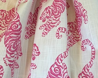 May include: A white fabric featuring a repeating pattern of tigers printed in a vibrant magenta pink. The material displays a visible woven texture with vertical and horizontal threads, and the fabric is draped to create soft, deep folds.