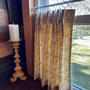 a window with a double pinch pleat curtain hanging from a rod, and a white candle on a wooden stand next to the curtain.