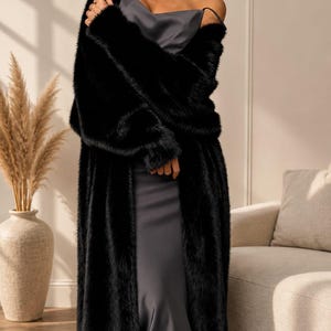 May include: A long, black faux fur coat with long sleeves and an open front, worn over a dark gray, sleeveless slip dress featuring a cowl neckline and thin shoulder straps that fall to a midi length.