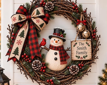 May include: A decorative wreath made of brown twigs featuring a central snowman figure wearing a black top hat and red and black plaid scarf. A large matching plaid bow, pinecones, red berries, two silver bells, and a sign reading The Smith Family.