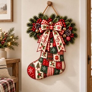 K&ouml;nnte beinhalten: Ein Weihnachtsstrumpf im Patchwork-Design aus roten, gr&uuml;nen und wei&szlig;en Quadraten mit Schneeflocken-, Tannenbaum- und Stechpalmenmotiven. Eine gro&szlig;e rot-wei&szlig; karierte Schleife oben ist mit dem Namen Sophia und dem Buchstaben S verziert.
