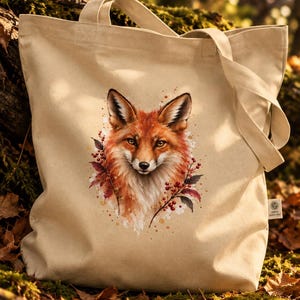 Könnte beinhalten: Eine beigefarbene Tragetasche aus Segeltuch mit einer Aquarell-Illustration eines Fuchskopfes auf der Vorderseite. Der Fuchs ist von roten Beeren und Herbstblättern umgeben. An der Seitennaht der Tasche befindet sich ein kleines Etikett.