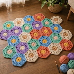 May include: A multi-colored crochet blanket composed of interconnected hexagonal motifs in shades of blue, orange, purple, green, and cream. Each hexagon features a central flower-like pattern. Several yarn balls and a crochet hook are nearby.