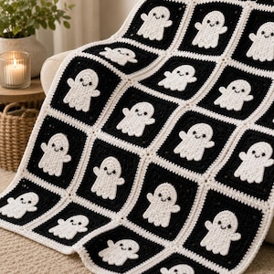 May include: A handmade crochet blanket featuring a repeating pattern of white ghost motifs centered on black square panels. The squares are joined together with a cream-colored yarn border, creating a grid-like structure across the entire textile.