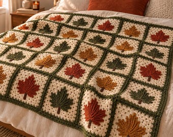 May include: A crochet blanket featuring a grid of square motifs, each containing a textured maple leaf in shades of rust, orange, and dark green. The leaves are centered on cream-colored backgrounds, framed by a dark green border.