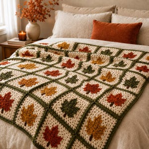 May include: A crochet blanket featuring a repeating square pattern, with each square containing a single leaf motif in shades of red, orange, and dark green. The background of each square is an off-white yarn, and the squares are joined by dark green borders.