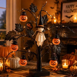 May include: A decorative Halloween tree with black branches, dark leaves, and small string lights. The tree features hanging orange jack-o'-lantern ornaments with black hats and a central white ghost figure wearing a black witch hat with an orange band.