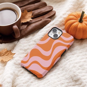 May include: A smartphone case featuring a repeating wavy pattern in alternating shades of orange and light pink. The case has a rectangular shape with rounded corners and a cutout for a dual-lens camera system on the upper left corner.