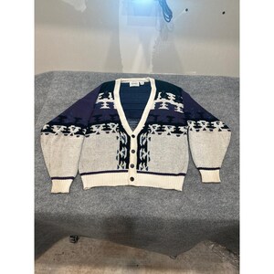 May include: A long-sleeve V-neck cardigan sweater featuring a geometric pattern in navy blue, dark purple, and cream. The garment has a button-front closure with four dark buttons and ribbed cuffs and hem, showcasing a repeating abstract design.