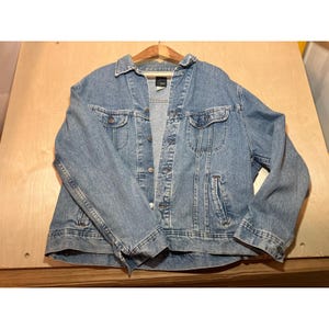 May include: A light blue denim jacket featuring a classic collar, long sleeves, and a front button closure. The jacket includes two chest pockets with buttoned flaps and two vertical side pockets. A Lee brand label is visible at the inner neck.
