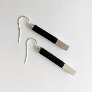 May include: A pair of black and silver earrings with a simple, modern design. The earrings are made of two rectangular pieces, one black and one silver, joined together. The earrings are suspended from silver hooks.