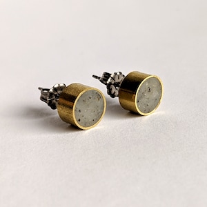 May include: A pair of gold stud earrings with a round, gray concrete inlay. The earrings have a silver post and butterfly backing.