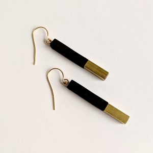 May include: A pair of black and gold earrings with a long, rectangular shape. The earrings are made of wood and metal.