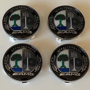 May include: Four circular wheel center caps featuring the Affalterbach crest with a black, white, and silver color scheme. Each cap displays a tree on the left, a valve-like symbol on the right, and the AMG logo in silver at the bottom edge.