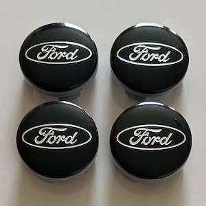 Pode incluir: Um conjunto de quatro tampas de centro de roda circulares com acabamento em preto brilhante e o logótipo Ford prateado em relevo no centro. Cada tampa tem uma superfície lisa e arredondada com uma borda oval em torno da marca.