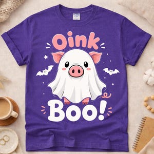 Peut inclure: Un t-shirt violet à manches courtes avec un motif représentant un cochon portant un drap de fantôme blanc. Le texte Oink est imprimé en rose au-dessus du cochon, et le mot Boo! est imprimé en blanc en dessous. Deux petites chauves-souris blanches et des étoiles entourent le cochon.