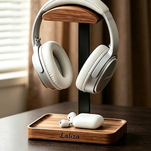 May include: A headphone stand featuring a dark wood base with the text Laliza, a black vertical support, and a curved wood top piece. White over-ear headphones rest on the top, while white wireless earbuds and a charging case sit on the base.