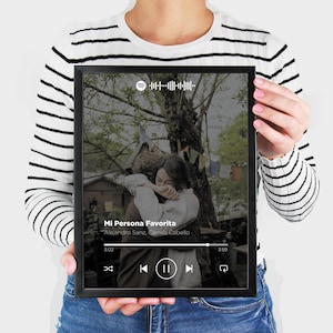 Puede incluir: Un marco rectangular negro con una impresión que muestra una interfaz de reproductor de música estilo Spotify sobre una foto de dos personas abrazándose. El texto dice Mi Persona Favorita de Alejandro Sanz, Camila Cabello.