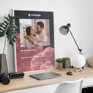 Puede incluir: Un cuadro decorativo rectangular con marco que presenta una interfaz de reproductor de música estilo Spotify. El diseño incluye una fotografía central de una pareja abrazada, superpuesta sobre un fondo de nubes rosas con el texto Me enamoré de ti de David Bisbal.