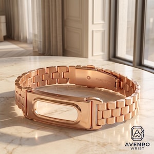 May include: A rose gold-toned stainless steel watch band featuring a polished rectangular frame for a fitness tracker. The link-style bracelet includes a secure folding clasp with the text STAINLESS STEEL engraved on the interior metal surface.