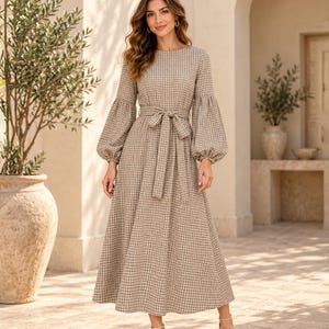 May include: A long-sleeved midi dress in a beige and black grid pattern. The dress features a round neckline, voluminous bishop sleeves with fitted cuffs, and a matching fabric tie belt at the waist, falling to a full, A-line skirt silhouette.