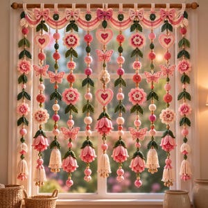 Puede incluir: Una cenefa de ventana de ganchillo decorativa con hilos colgantes de flores, corazones y mariposas en rosa y blanco. La cenefa cuelga de una barra de madera e incluye hojas verdes, cuentas esféricas y borlas en tonos rosa y blanco.