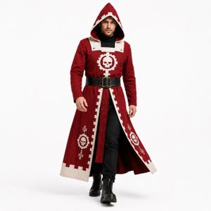 Pu&ograve; includere: Un lungo cappotto con cappuccio rosso scuro, caratterizzato da bordi bianchi e un emblema bianco a forma di ingranaggio con un teschio al centro sul petto e sui pannelli inferiori. Il cappotto include una cintura nera con fibbia rettangolare.