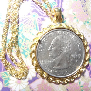 May include: A gold-toned necklace featuring a United States quarter coin pendant. The coin is set in a decorative gold frame with a rope-like border. The chain is also gold and has a twisted design.