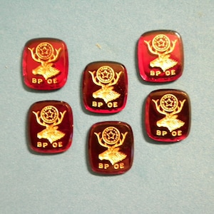 May include: Six rectangular, red glass pieces with a gold emblem of a deer head and a star. The text "BP OE" is below the deer. The pieces are arranged on a light blue surface.