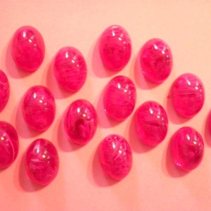 Może przedstawiać: Kolekcja piętnastu owalnych, błyszczących kaboszonów w kolorze fuksji. Każdy kaboszon ma półprzezroczysty, marmurkowy wygląd z białymi wirami. Kaboszony ułożone są na jasno-różowej powierzchni.